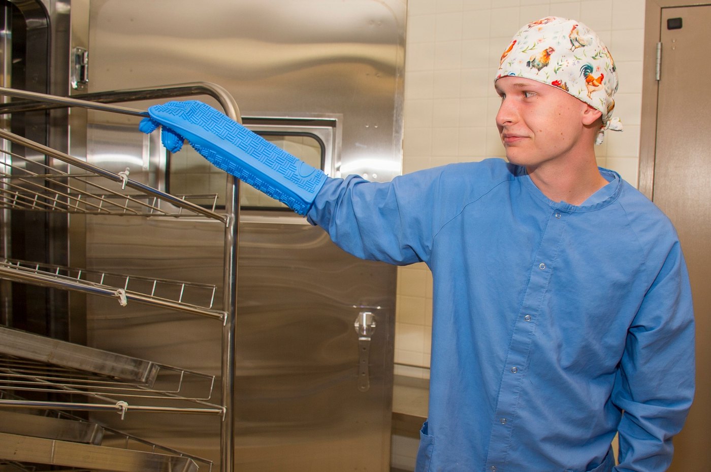 Operator handling a metal rack beside a hospital cart washer